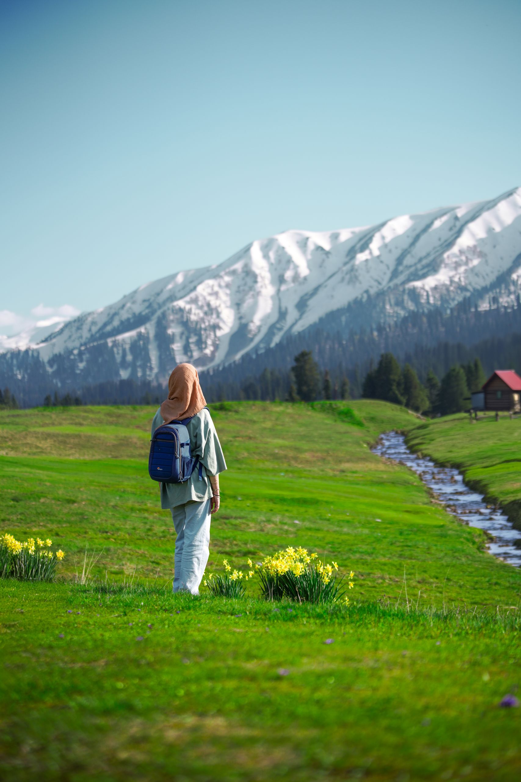 A woman with a backpack enjoys the scenic view of snowcapped mountains in Gulmarg, Jammu and Kashmir.